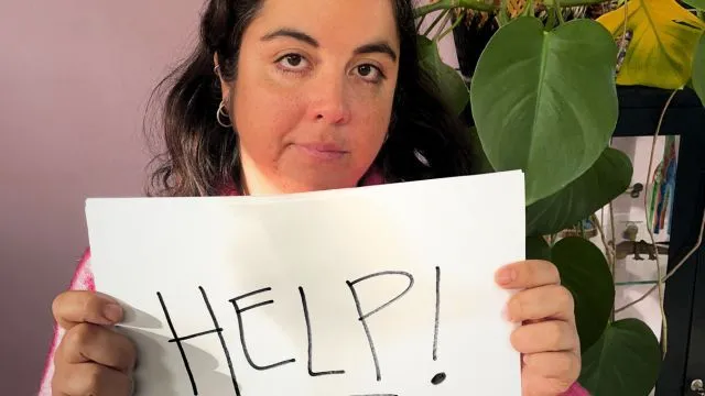 Maria Montserrat holding a hand-written sign that reads HELP!