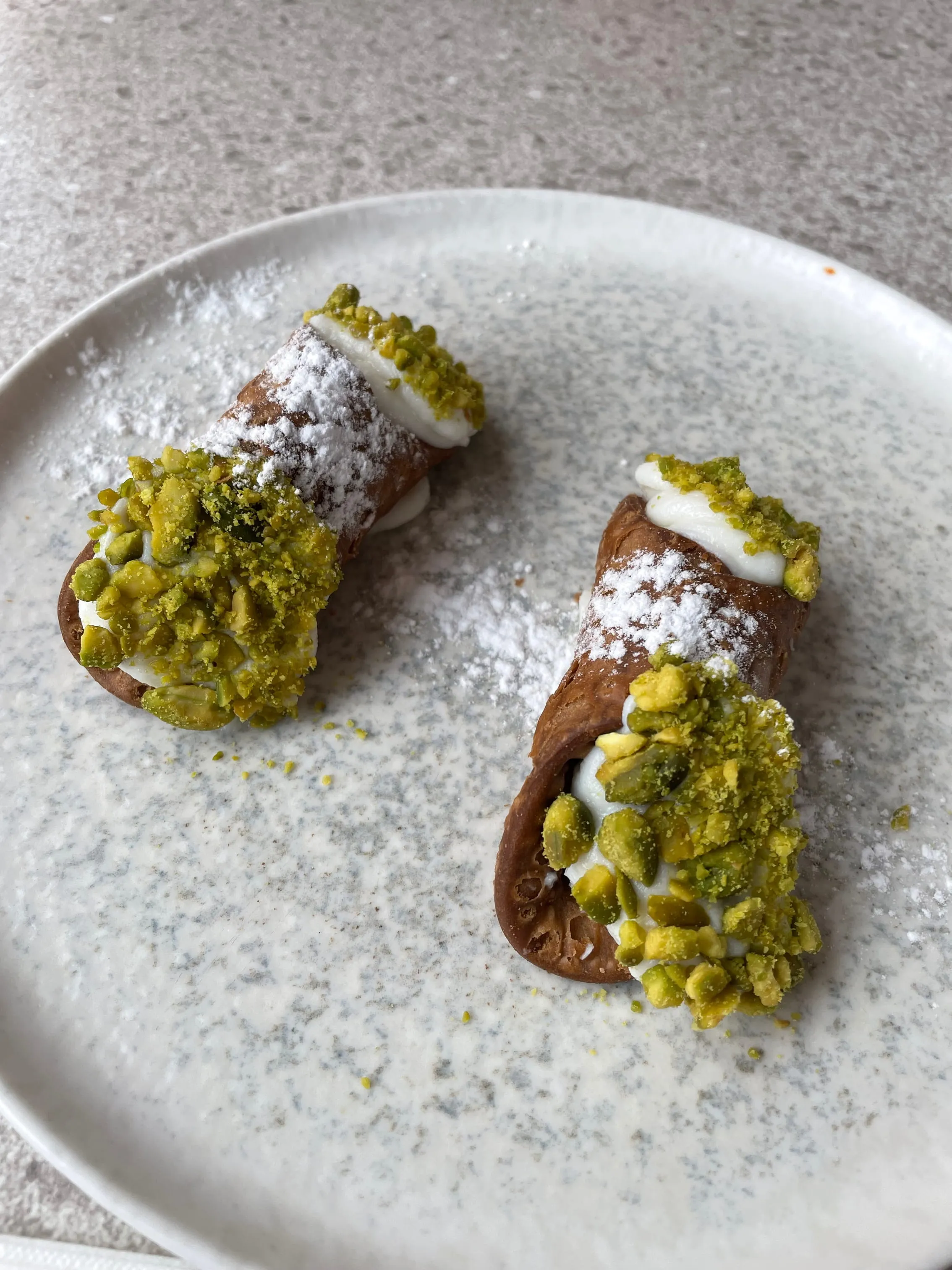 Food photograph — pistachio cannoli dusted with powdered sugar